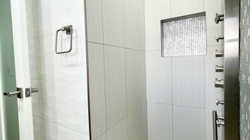 Un espace douche moderne doté d’une porte en verre, d’un pommeau de douche à main et d’un sol carrelé.