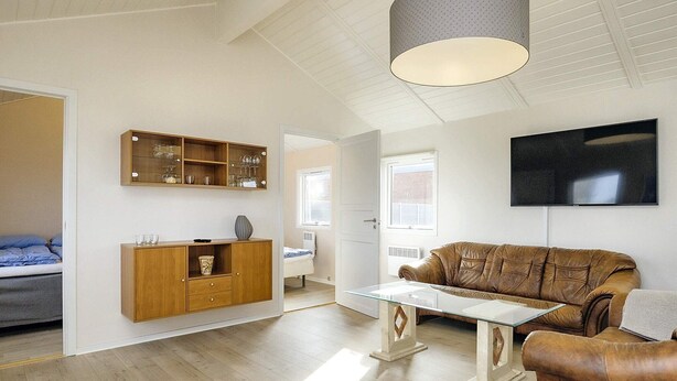 A modern living room with a leather sofa, a glass coffee table, and a wooden cabinet with glassware.