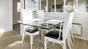 A dining area with a glass table, white wicker chairs with black cushions, and a modern pendant light.