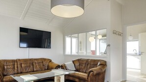 A modern living room with leather sofas, a glass coffee table, and a large TV on the wall.