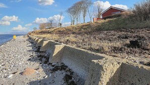 A coastal scene with a concrete sea defense, a red building, and leafless trees.