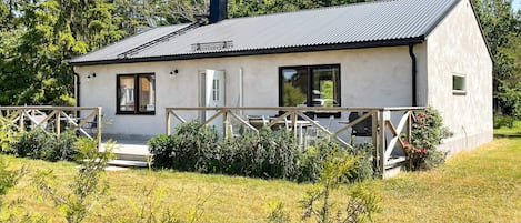 A single-story building with a flat roof, a chimney, and a small porch with a railing.