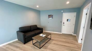 A room with a dark grey sofa, a wooden coffee table, and a white door with a peephole.