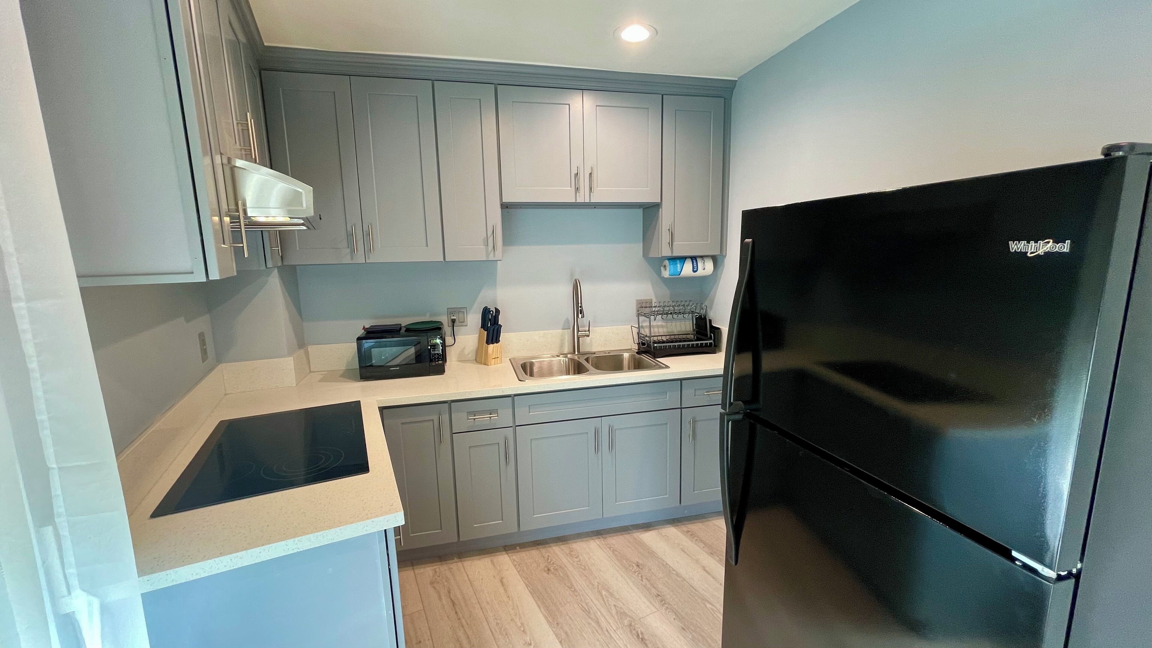 A modern kitchen with grey cabinets, a black refrigerator, a microwave, and a sink.