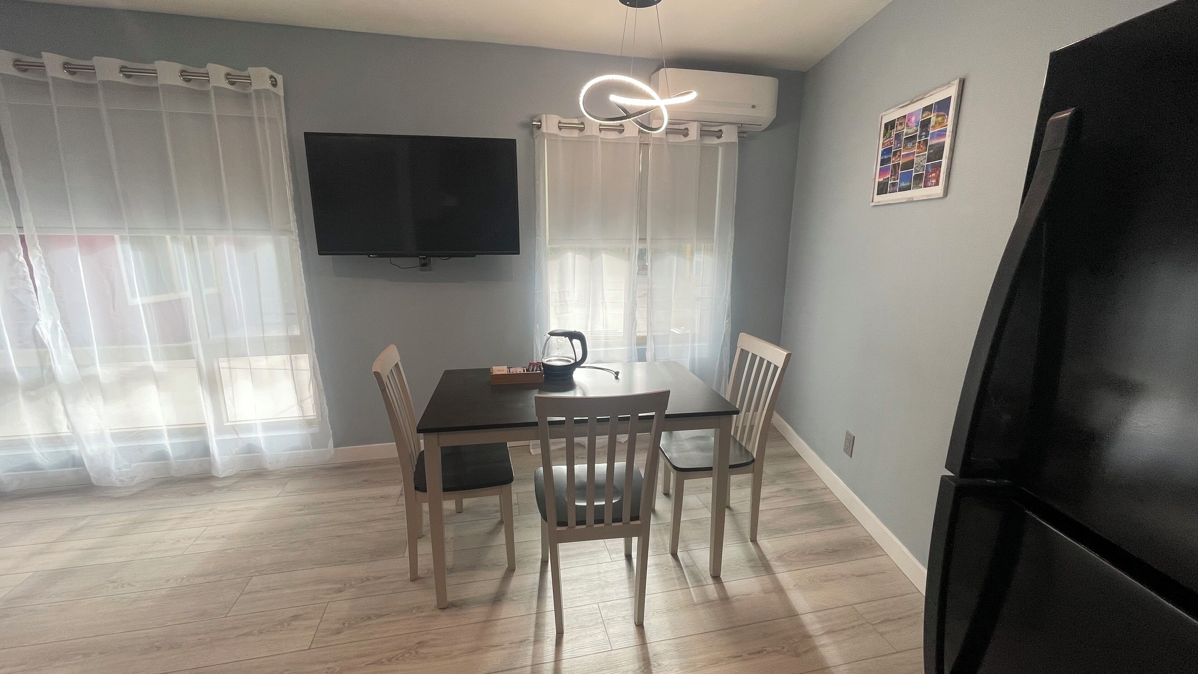 A dining area with a table, chairs, a kettle, and a television on the wall.