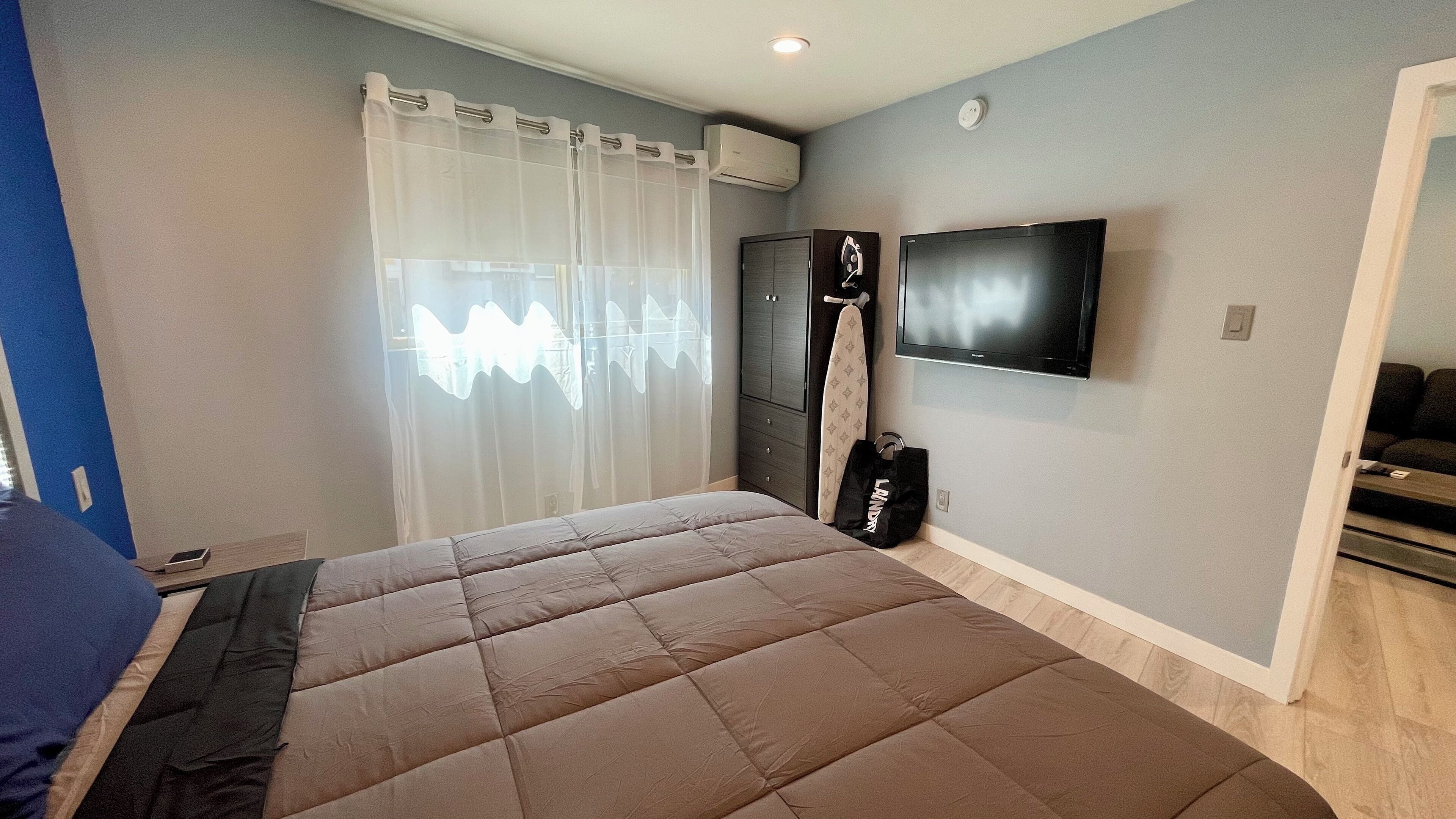 A bedroom with a large bed, a TV mounted on the wall, and a wardrobe.