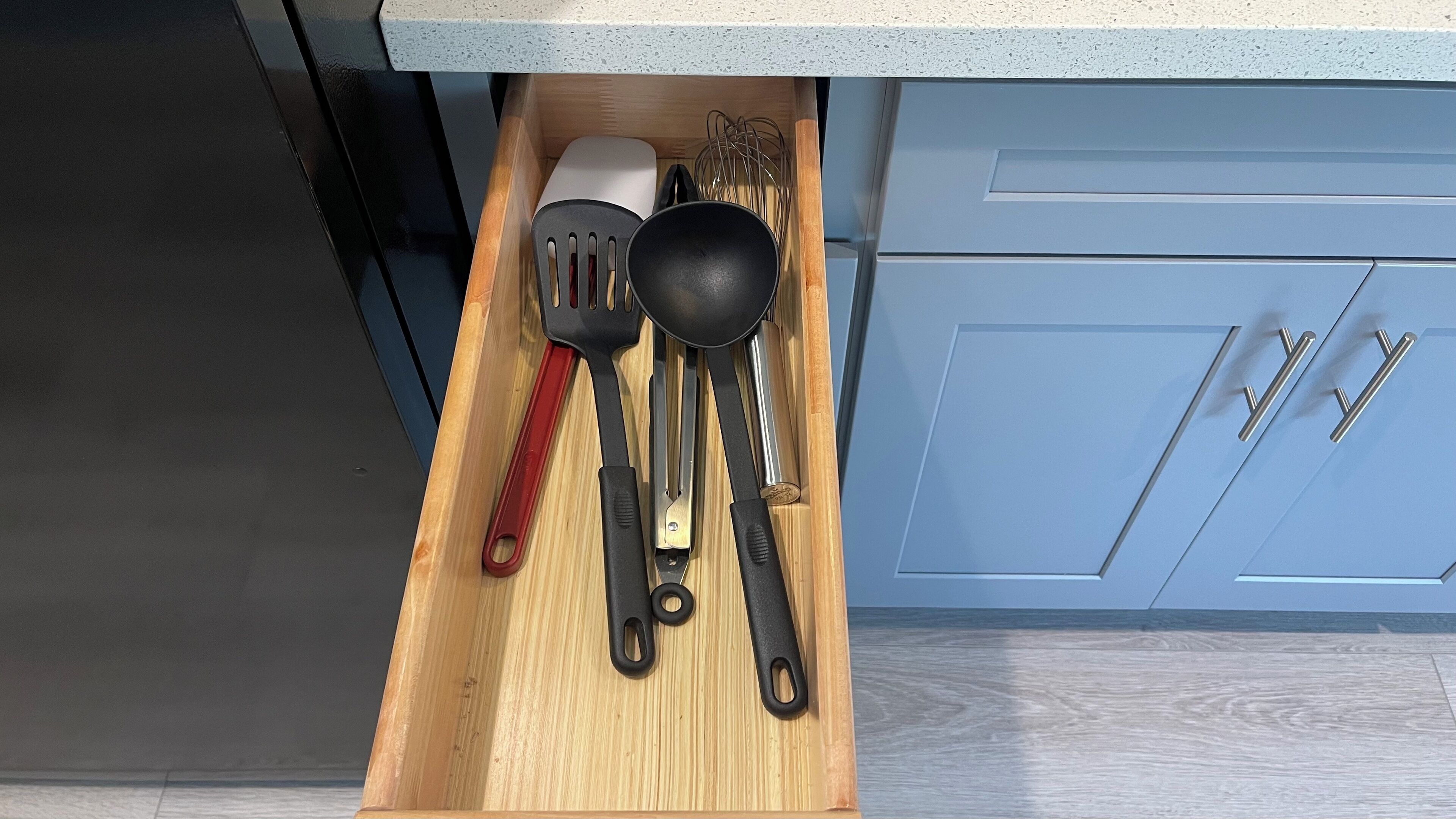 Un cajón de cocina con utensilios, incluyendo una espátula, una cuchara escurridora y un par de pinzas.