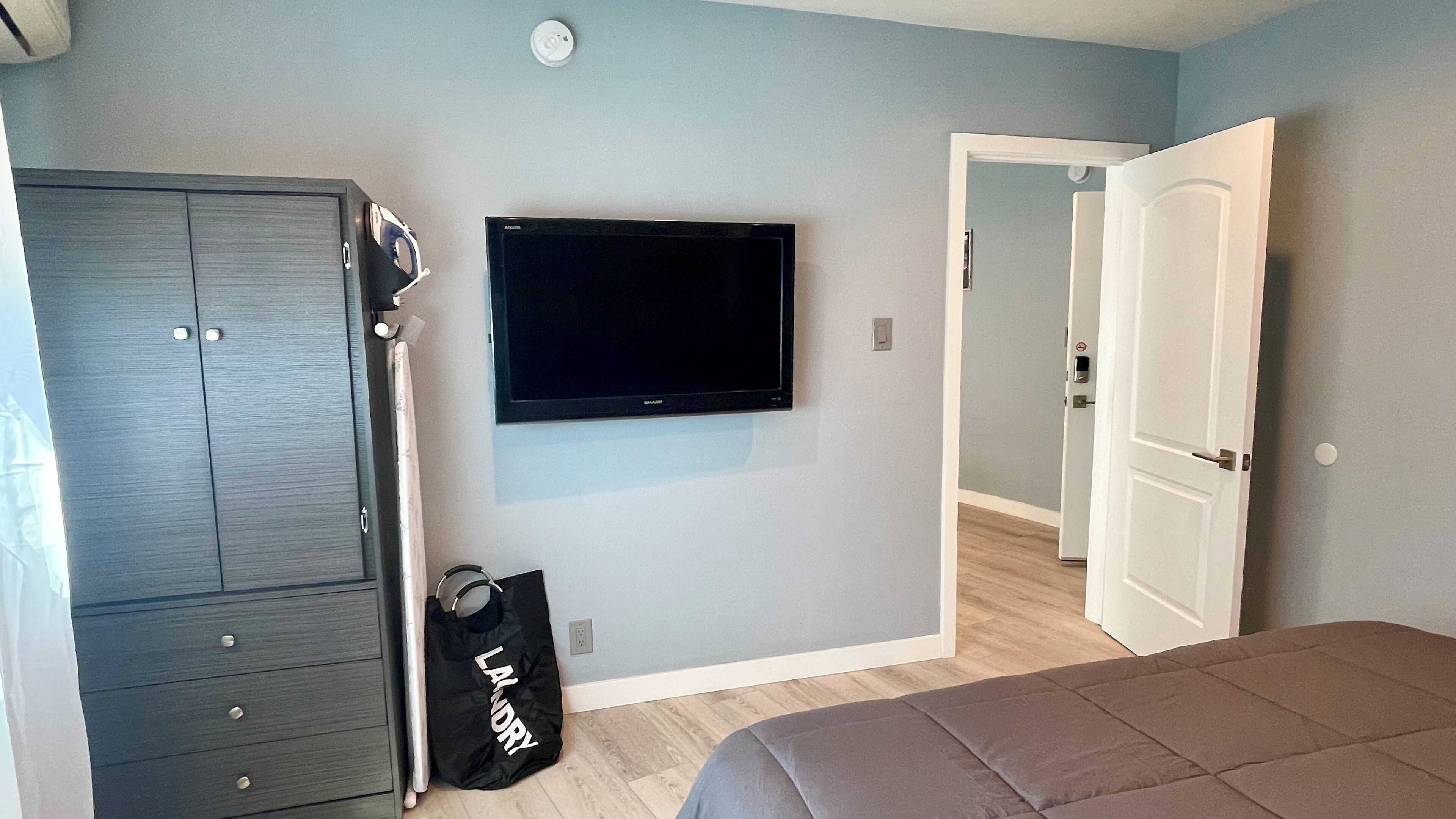 A bedroom with a bed, a wardrobe, a television, and a door leading to another room.