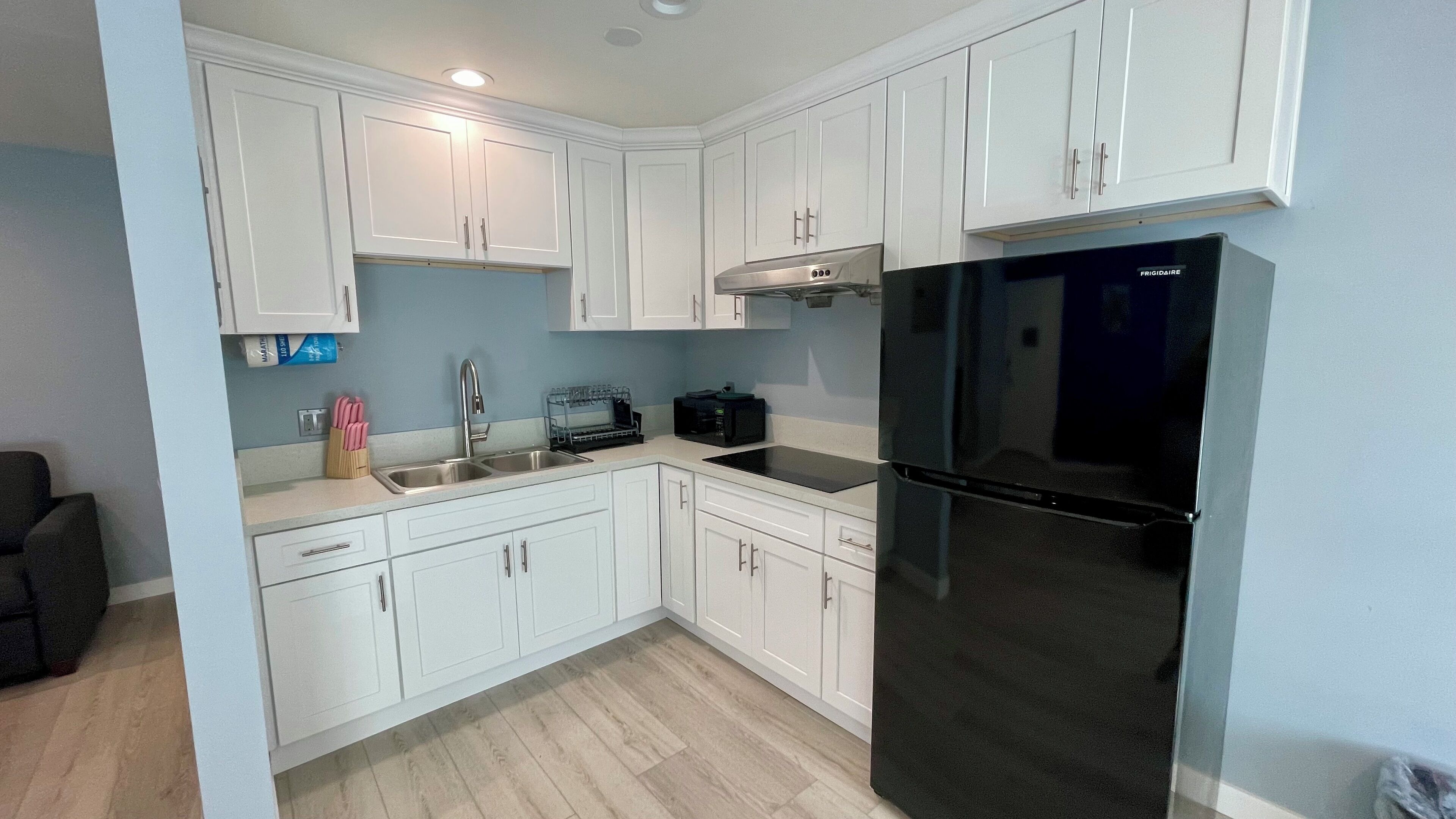 A modern kitchen with white cabinets, a black refrigerator, and a microwave.