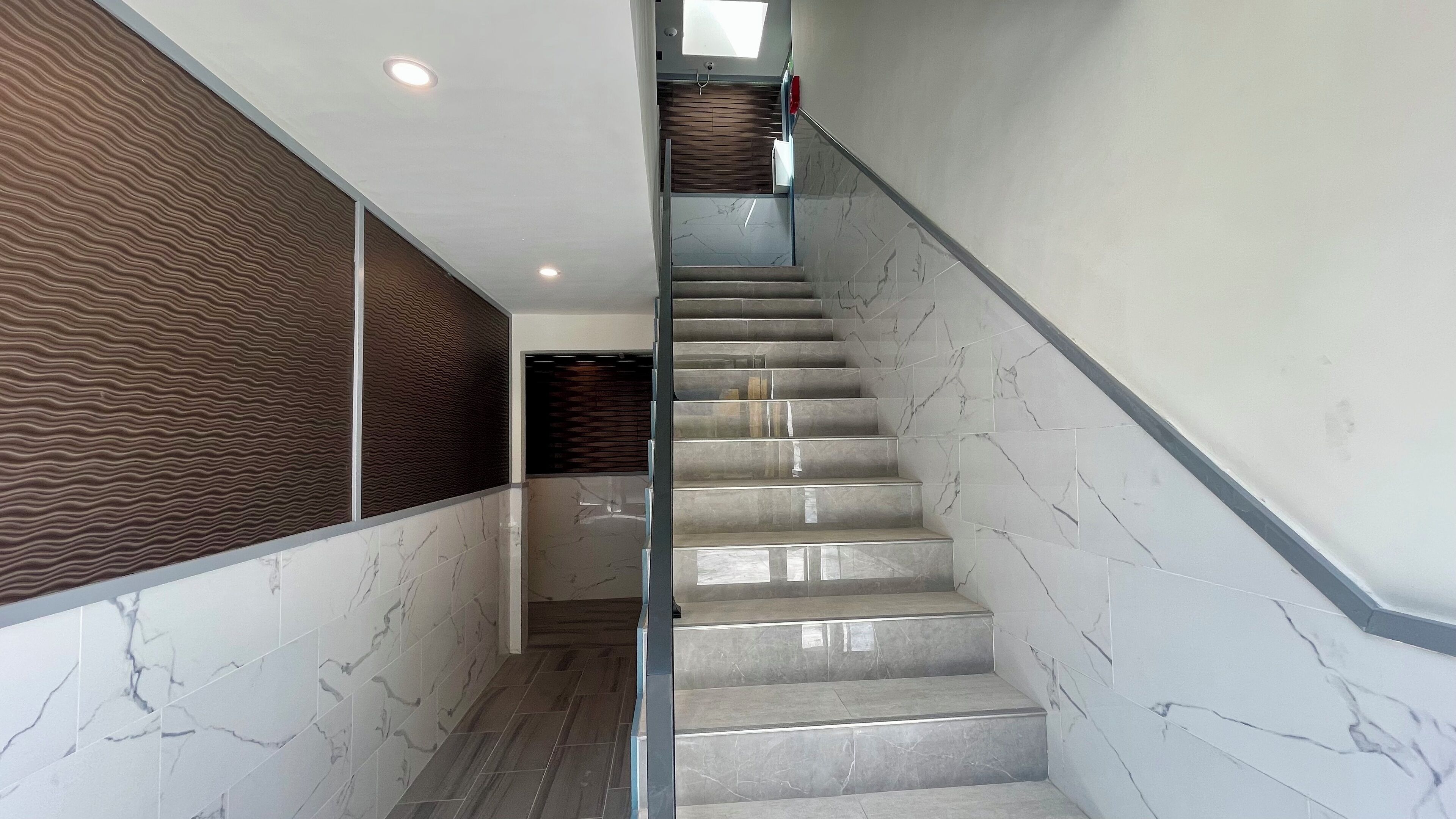 A modern staircase with marble steps and a glass railing, leading to a landing with a patterned wall and a door.