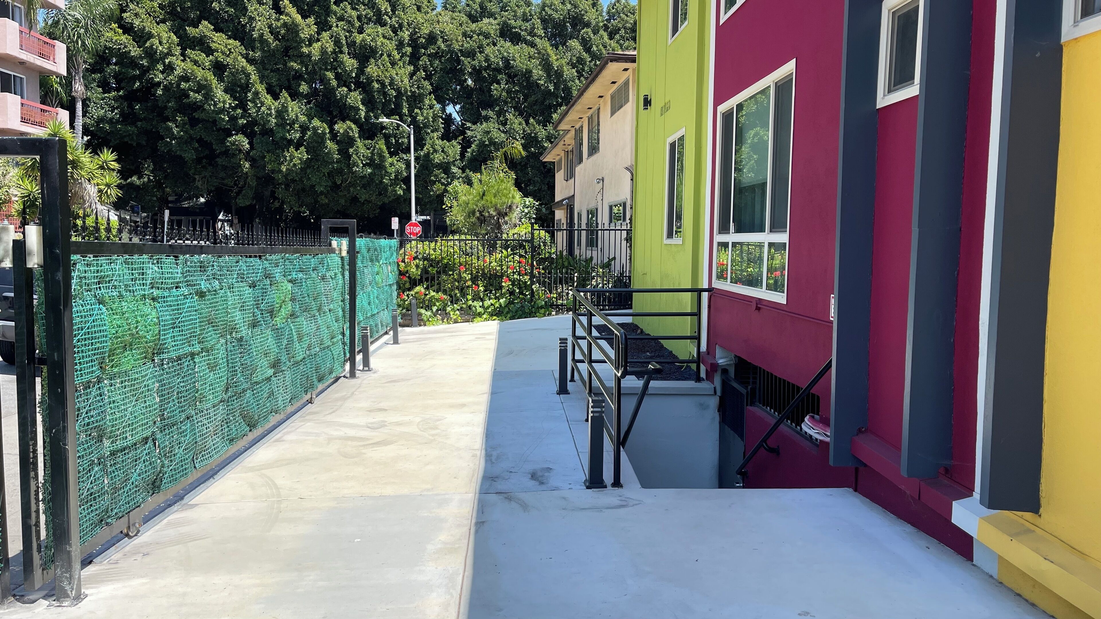 A narrow pathway leading to a building with colorful facades, a green fence, and a stop sign.