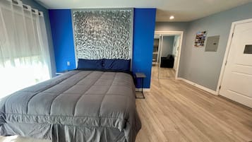Ein Schlafzimmer mit einem großen Bett, einem Kopfteil mit geometrischem Muster, einem Nachttisch und einer Tür zu einem anderen Raum.