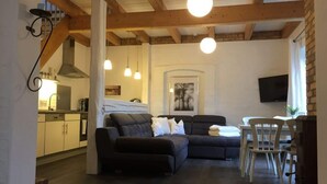 A modern living room with a sofa, a dining area with chairs, and a kitchen in the background. - Holiday Home Grussow (Fuenfseen)