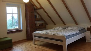 A bedroom with a sloped ceiling, a bed, a window, a brick fireplace, and a green chair. - Holiday Home Grussow (Fuenfseen)
