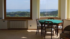 A dining area with a table and chairs, large windows with a view of the landscape, and a radiator on the wall. - Belvilla by OYO Villa Degli Olivi (Grotte di Castro)