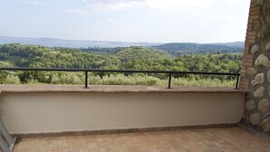 A balcony with a stone wall and a metal railing overlooking a forested landscape. - Belvilla by OYO Villa Degli Olivi (Grotte di Castro)