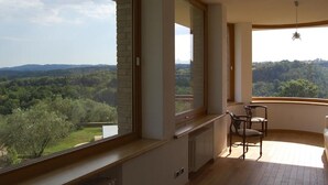 A room with large windows offering a view of a forested landscape. - Belvilla by OYO Villa Degli Olivi (Grotte di Castro)