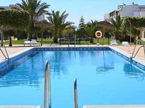 A rectangular swimming pool with clear blue water, surrounded by a tiled deck. There are palm trees and a fence in the background. - Duplex in Urb Naturista Near Beach & Pool (Vera)