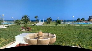 A landscaped area with a fountain, palm trees, and a pool in the background. - Duplex in Urb Naturista Near Beach & Pool (Vera)