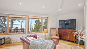 Ein Wohnzimmer mit einer Ledersofa, Holzboden, einem Fernseher und großen Fenstern mit Blick auf eine schöne Aussicht.