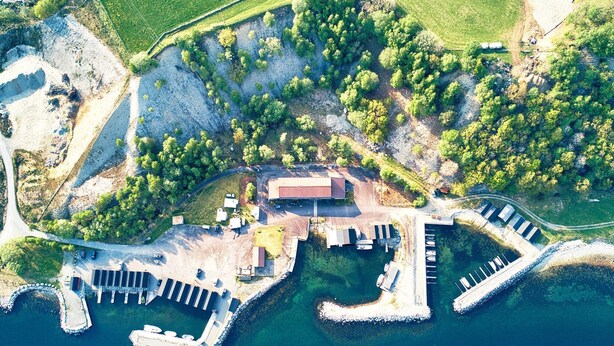 Vista aérea de una propiedad costera con un muelle, un edificio grande y vegetación circundante.