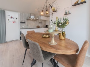A modern kitchen with a wooden dining table, grey upholstered chairs, and a pendant light fixture. - Detached House on Lake in Zeeland Holiday Park (Wemeldinge)