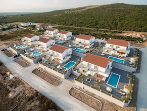 Vista aérea de um complexo residencial moderno com várias casas, cada uma com piscina e área de varanda.