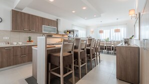 A modern kitchen with wooden cabinets, a central island with bar stools, and a dining area with a large table and chairs. - Nicely Decorated Villa With Swimming Pool (Sukosan)