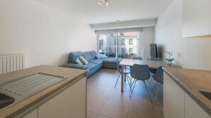 A modern apartment with a kitchen, dining area, and living space. It features a large window, a sofa, and a TV.