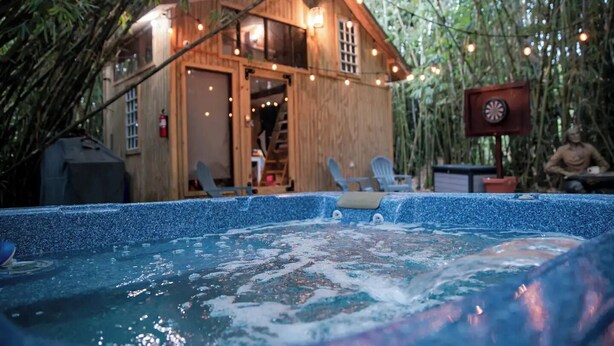 A hot tub area with a wooden cabin and string lights, surrounded by bamboo. - HW Tiny Home Cidra (Cidra)