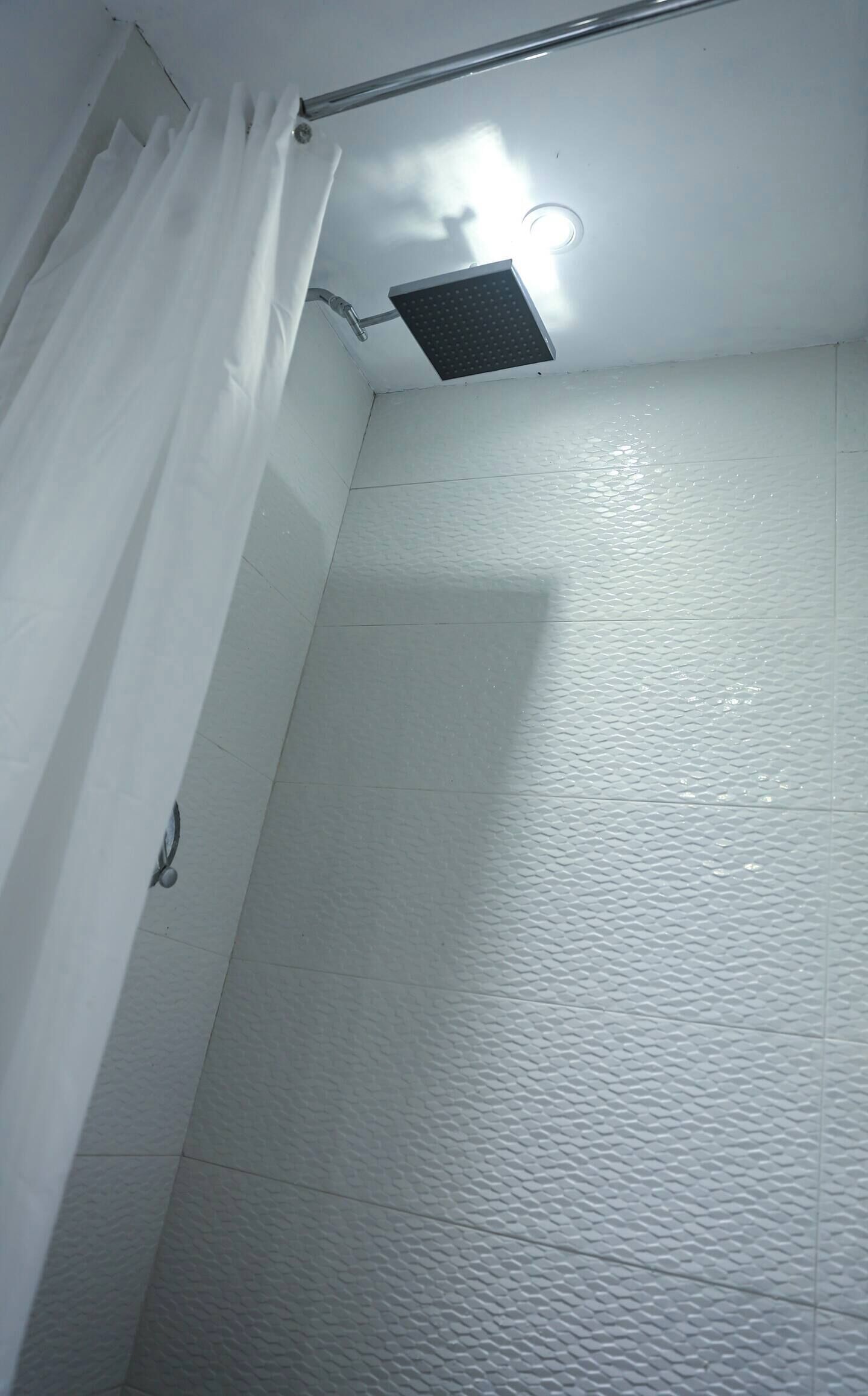 A shower area with a ceiling-mounted showerhead, white textured walls, and a curtain.