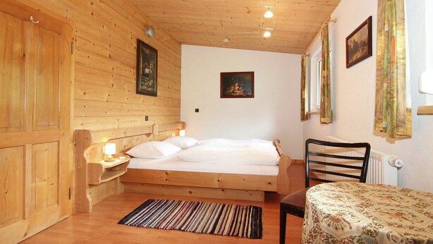 Ein Zimmer in einer Holzhütte mit einem Bett, einem Tisch und einem Stuhl.