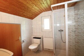 Un baño con inodoro, ducha con puerta de vidrio y ventana sobre el inodoro.