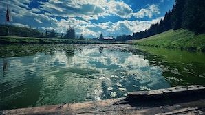 Ein ruhiger Fluss mit Spiegelungen des Himmels und der Bäume, umgeben von viel Grün und einer Holzsteganlage.