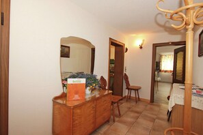 A dining area with a wooden cabinet, a chair, a table with a white tablecloth, and a mirror reflecting the room.