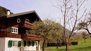 Ein zweigeschossiges Holzhaus mit einem Balkon, umgeben von einer Rasenfläche und Bäumen.