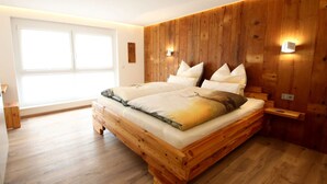 A bedroom with a wooden bed frame, two bedside tables, and a large window. - Holiday Apartment Holzwieb (Unterkirnach)