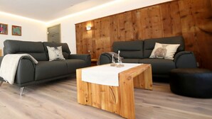 A modern living room with two dark grey sofas, a wooden coffee table, and a wooden accent wall. - Holiday Apartment Holzwieb (Unterkirnach)