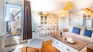 A modern living room with a sofa, a dining table, and a kitchen area. - Coastal Retreat With Balcony (Koksijde)