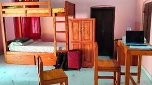 Une chambre avec un lit superposé, un bureau avec un ordinateur portable, une chaise, une armoire et une valise.