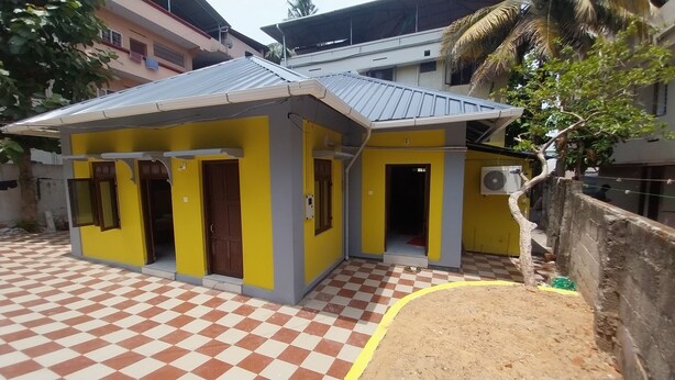 Un petit bâtiment jaune avec un sol à carreaux, une porte et une fenêtre.
