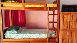 Un lit superposé avec une tête de lit en bois, un lit inférieur recouvert d’une couvre-lit à motifs floraux et une armoire en bois à deux portes.