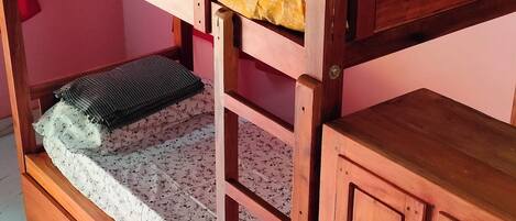 A bunk bed with a wooden frame, a lower bed with a floral mattress, and a cabinet with drawers.
