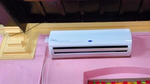 Un appareil de climatisation blanc, posé sur une surface rose et doté d’un socle en bois.