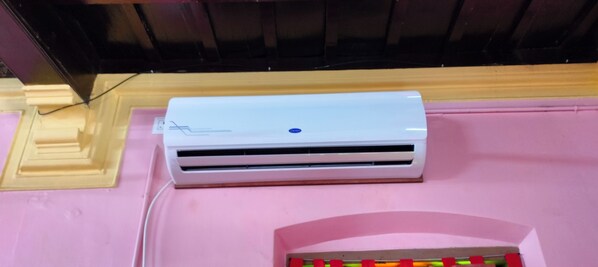 Un appareil de climatisation blanc, posé sur une surface rose et doté d’un socle en bois.