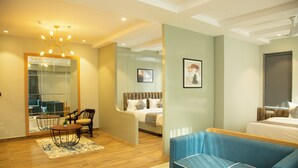 A modern hotel room with a bed, a blue sofa, a dining table with chairs, a large mirror, and a ceiling light fixture. - Cosmos Westend City Centre (Udaipur)