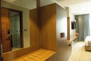 A hotel room with a wooden wardrobe, a mirror, a bed, and a television.