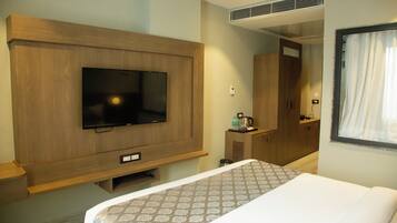 Habitación de hotel con cama, televisión montada en un panel de madera, kitchenette pequeña y espejo.