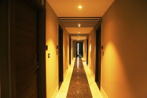 A hotel hallway with a polished floor, doors on both sides, and a light source at the end.