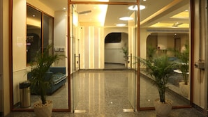 A hotel lobby with a glass door entrance, a blue sofa, and potted plants. - Cosmos Westend City Centre (Udaipur)